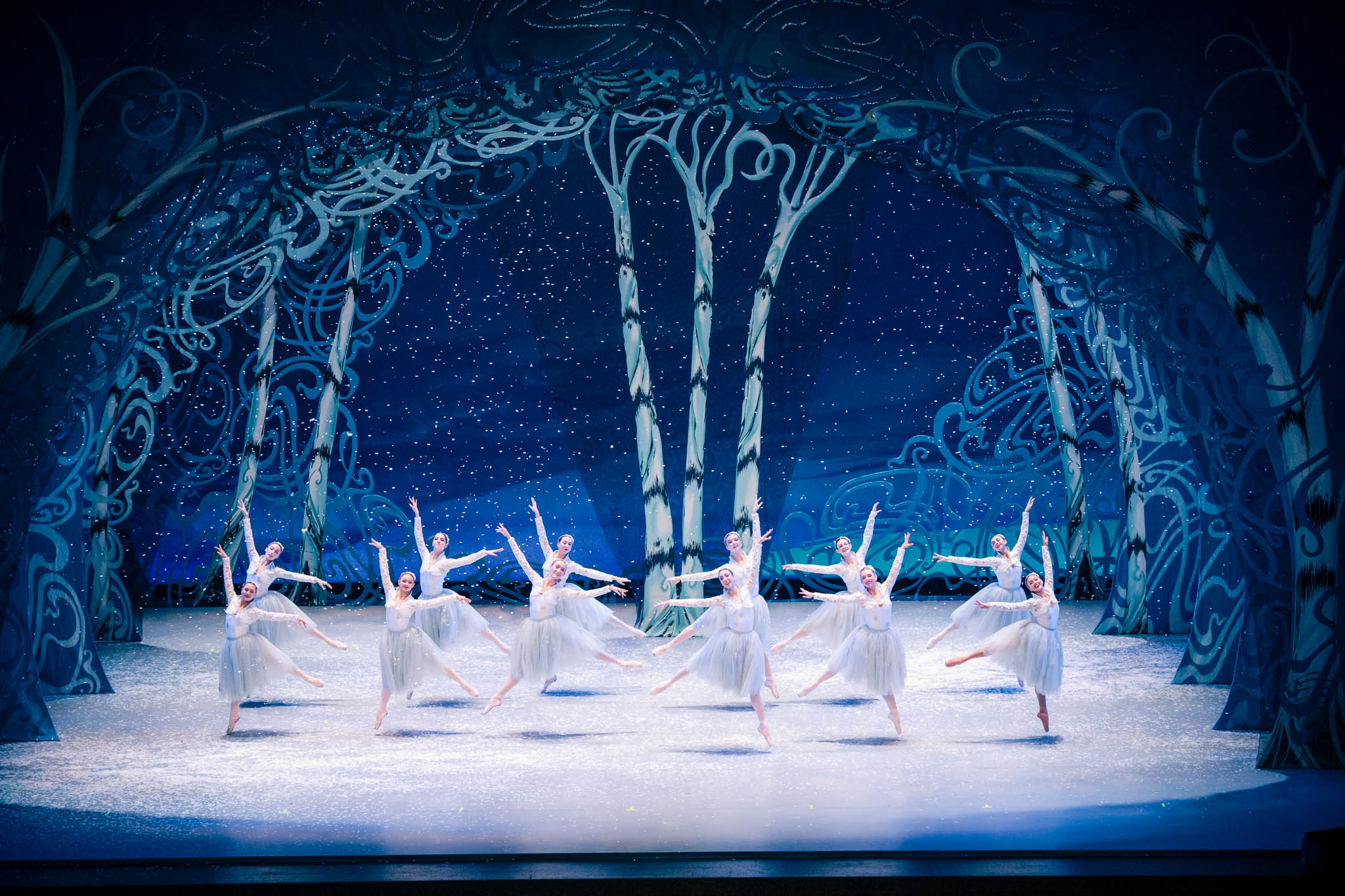 A stage full of ballerinas wearing white romantic tutus with a snowy forest background